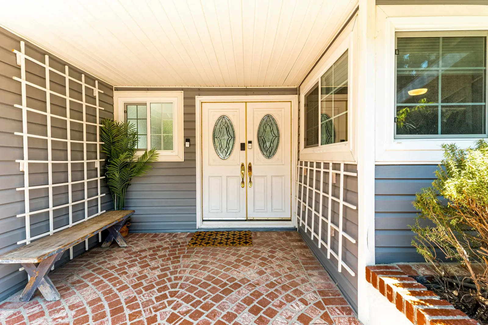 Welcoming residential porch with double doors and brick flooring.